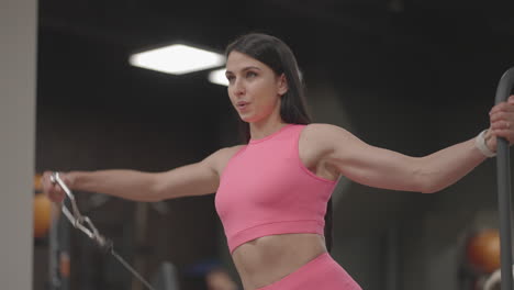A-young-woman-in-a-crossover-raises-her-shoulder-arms-in-a-pink-suit.-Exercises-for-training-the-arms-and-shoulders